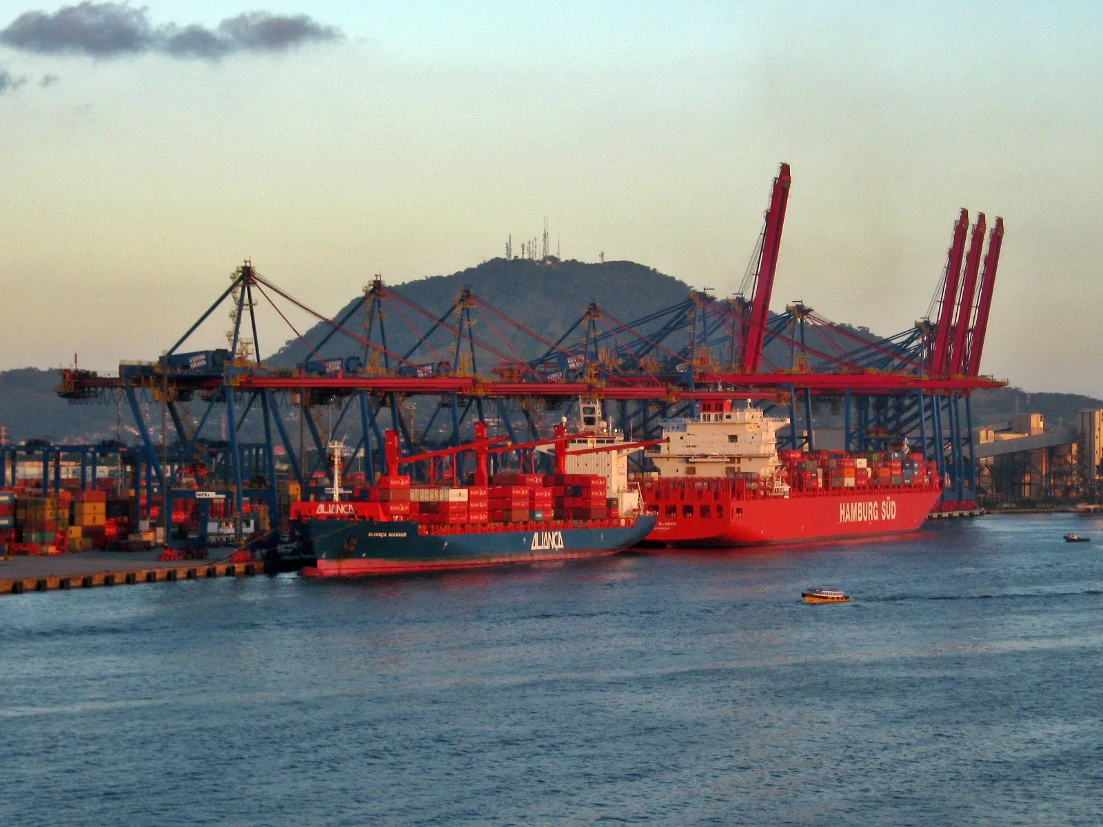 Navios de contêineres atracados no Porto de Santos, com guindastes vermelhos e pilhas de contêineres no cais.