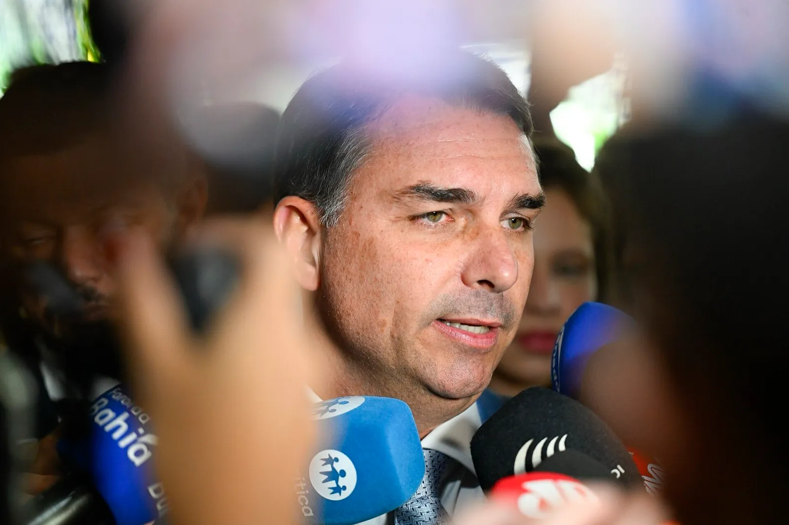 O senador Flávio Bolsonaro fala a jornalistas cercado de microfones, em close.