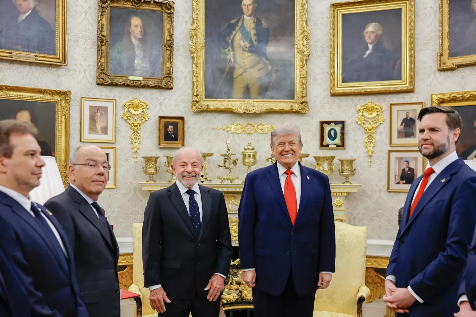 Lula, de terno escuro, e Donald Trump, de terno azul e gravata vermelha, em pé diante de quadros dourados numa sala da Casa Branca.