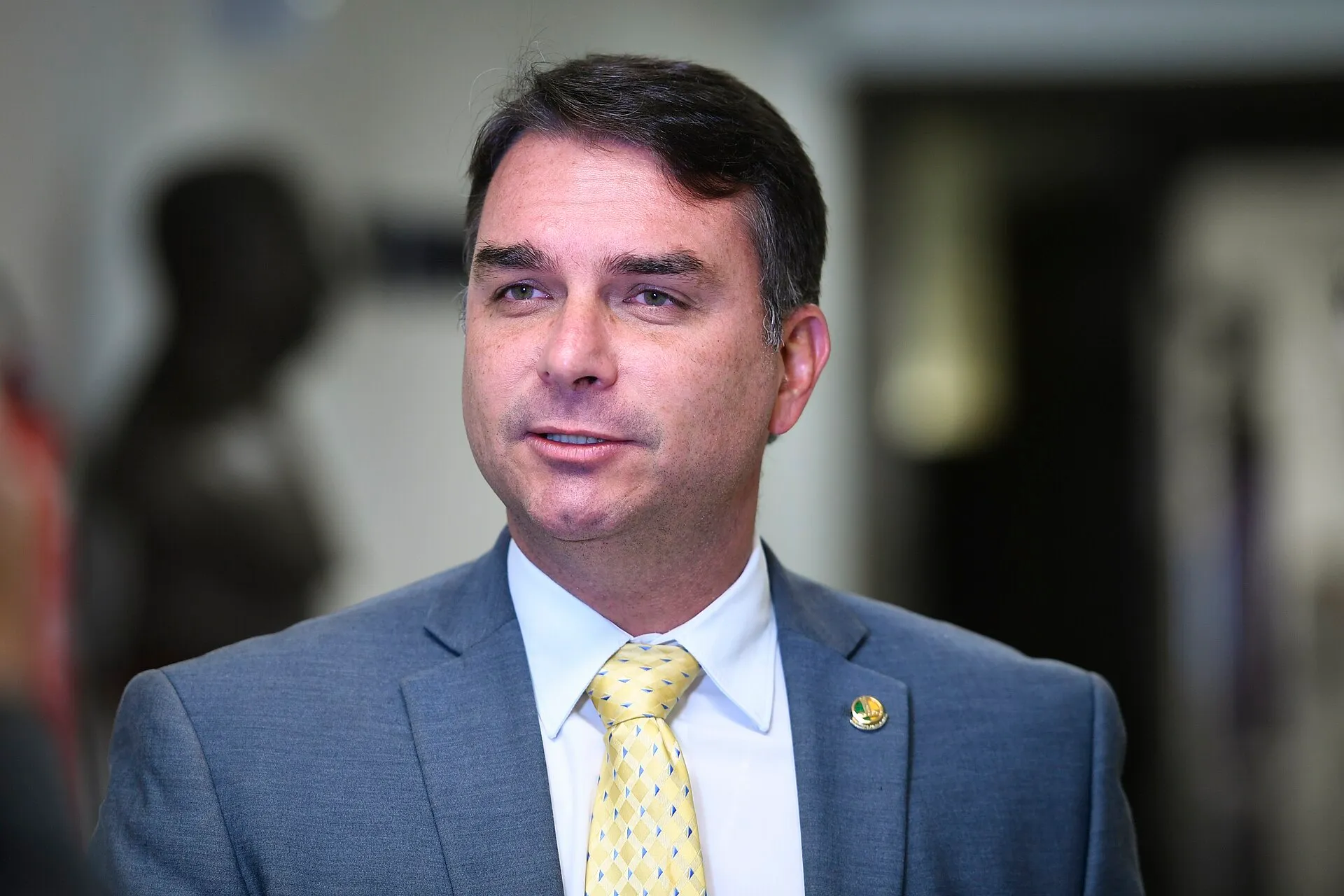Flávio Bolsonaro, de terno cinza e gravata amarela, concede entrevista no Senado Federal.