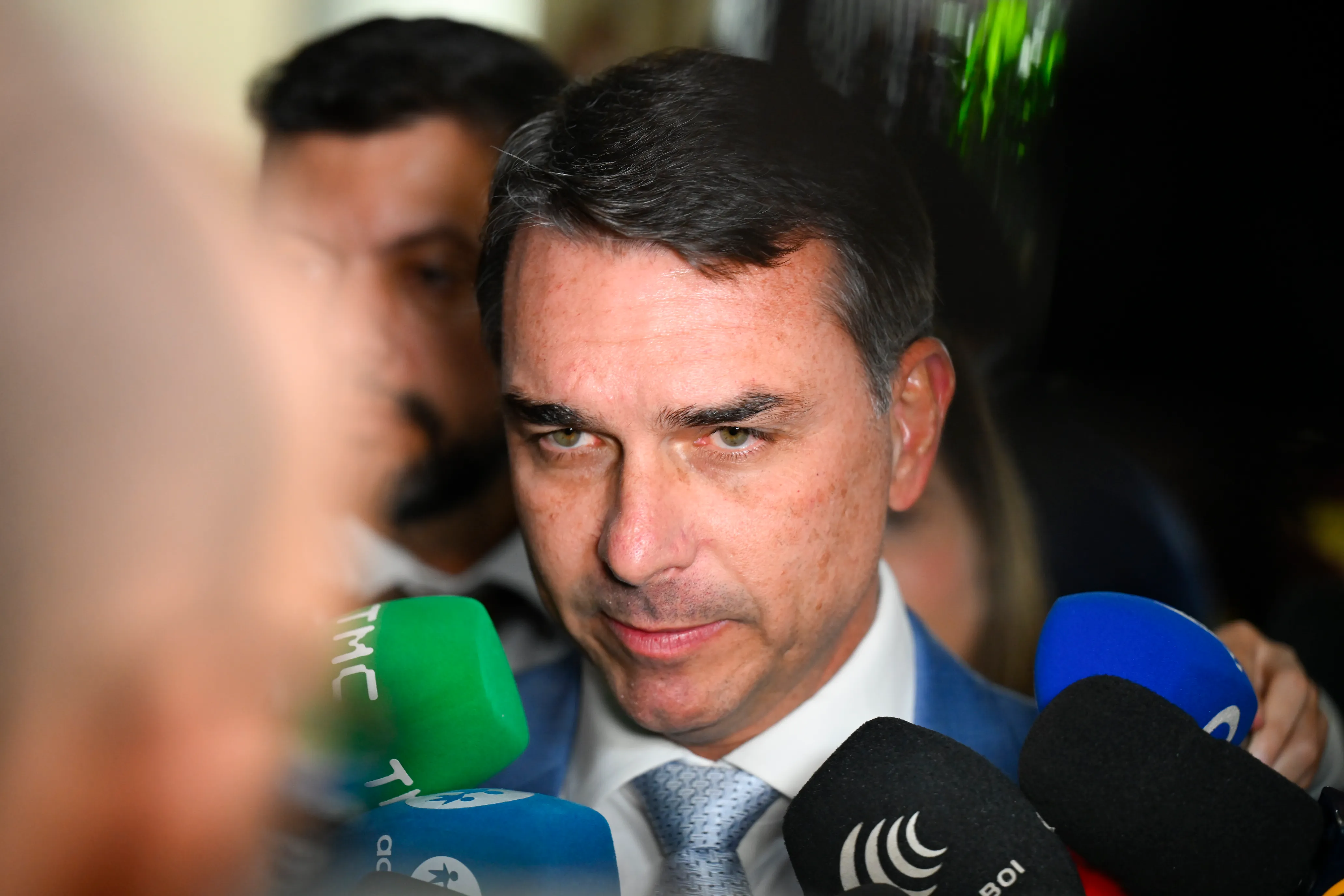 O senador Flávio Bolsonaro concede entrevista cercado por microfones.