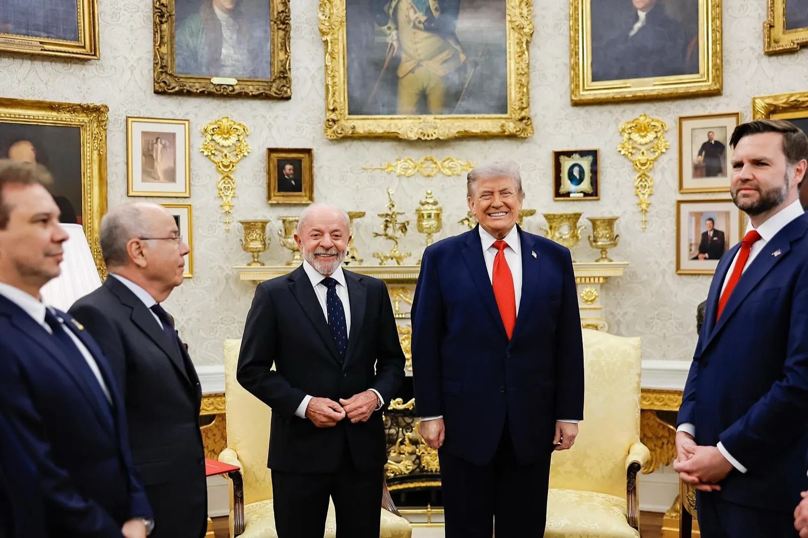 Lula, de terno escuro, e Donald Trump, de terno azul e gravata vermelha, sorriem no Salão Oval da Casa Branca, diante de quadros dourados e cadeiras amarelas.