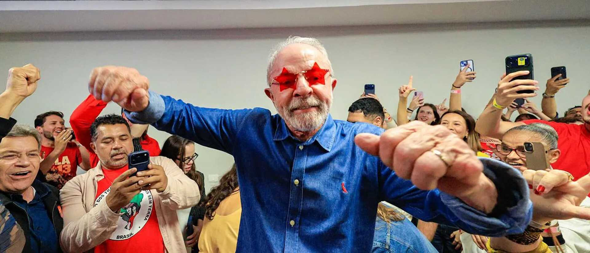 Lula, de camisa azul e óculos vermelhos, cumprimenta apoiadores durante discurso após a reeleição.