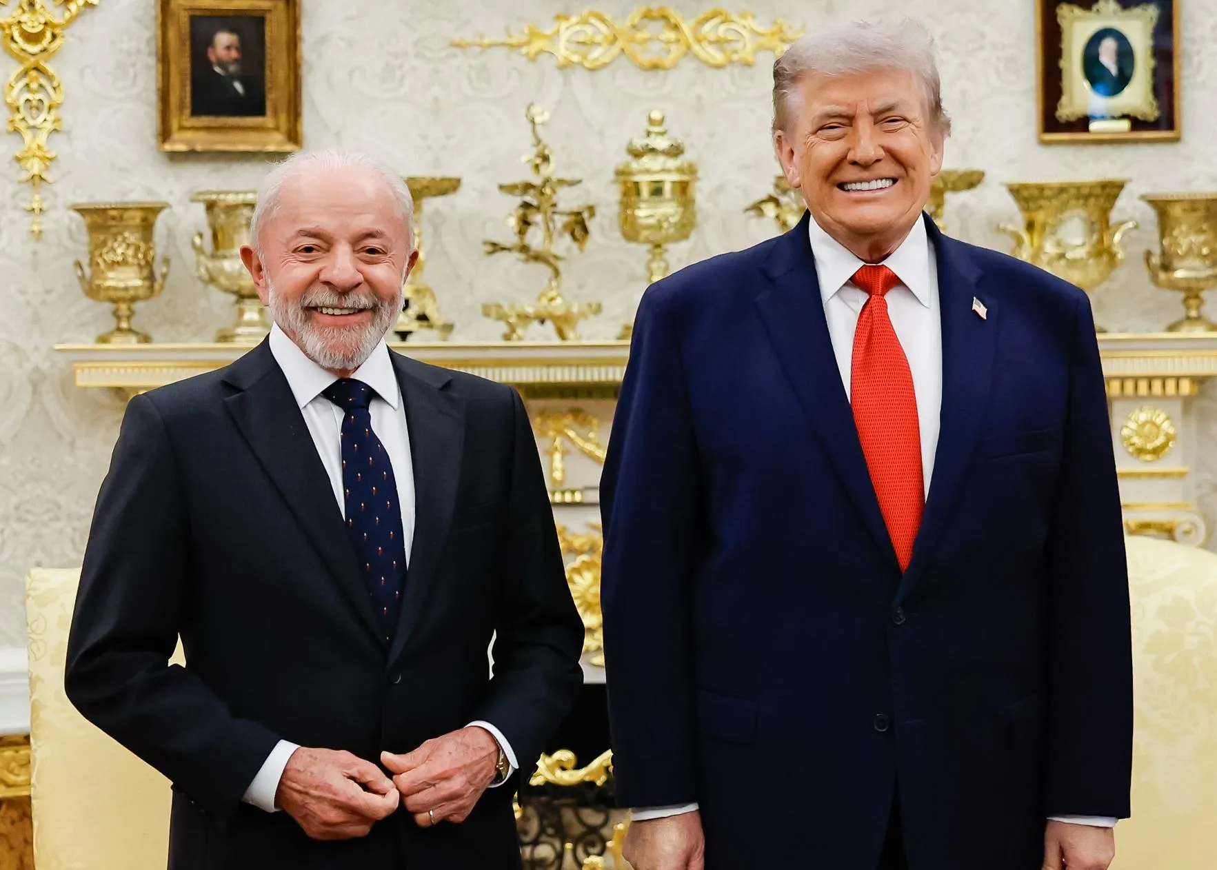 O presidente Lula e o presidente dos Estados Unidos, Donald Trump, lado a lado, sorrindo, em uma sala decorada com dourados na Casa Branca.