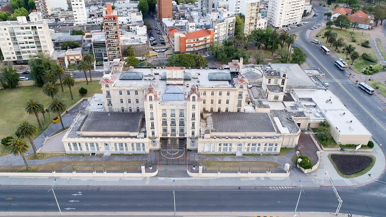 Vista aérea do edifício-sede do Mercosul em Montevidéu, com fachada clara, telhados e jardins ao redor.