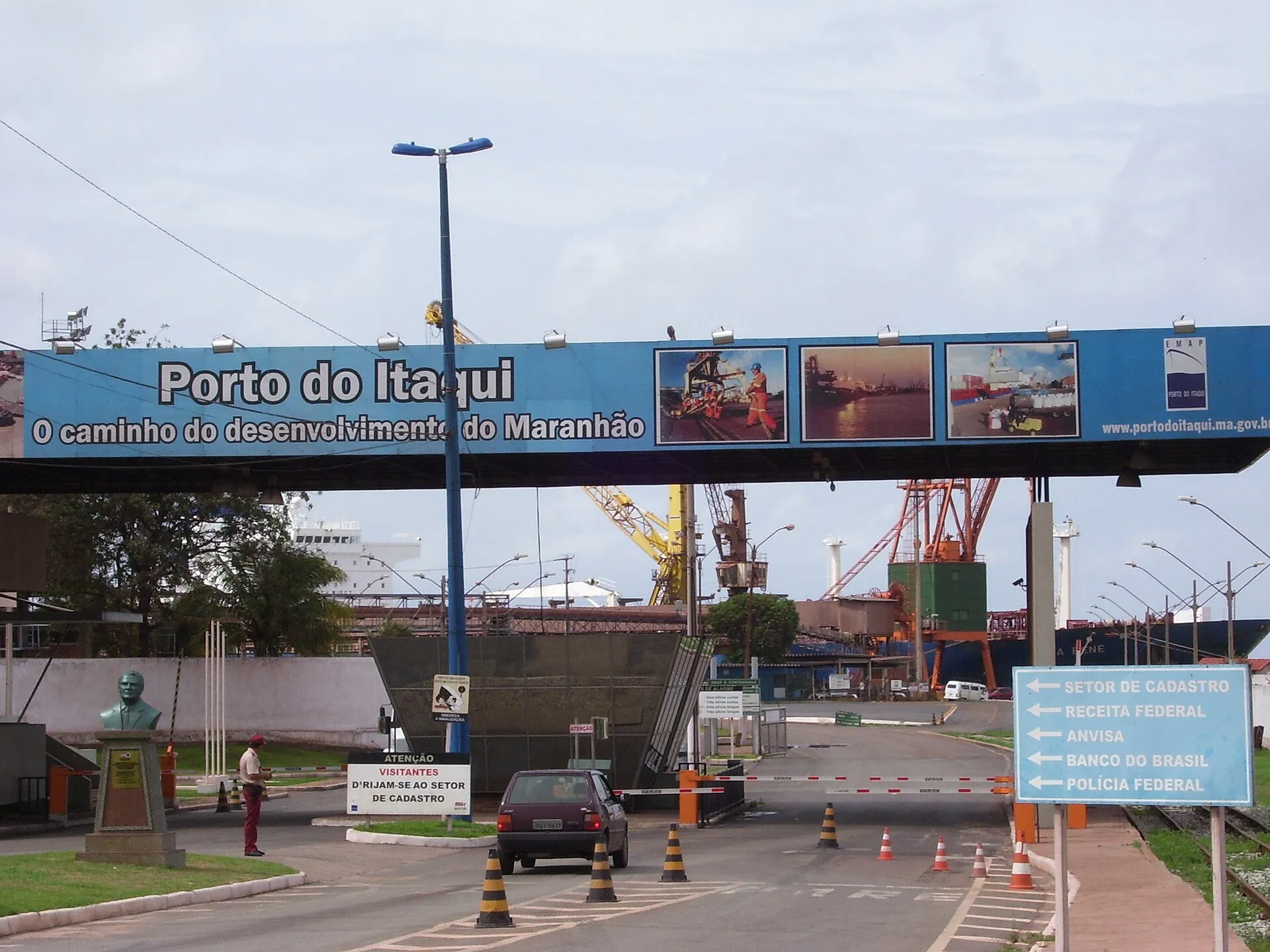 Portaria do Porto do Itaqui, em São Luís, com a faixa 'O caminho do desenvolvimento do Maranhão', guindastes e um navio ao fundo e um carro na cancela.