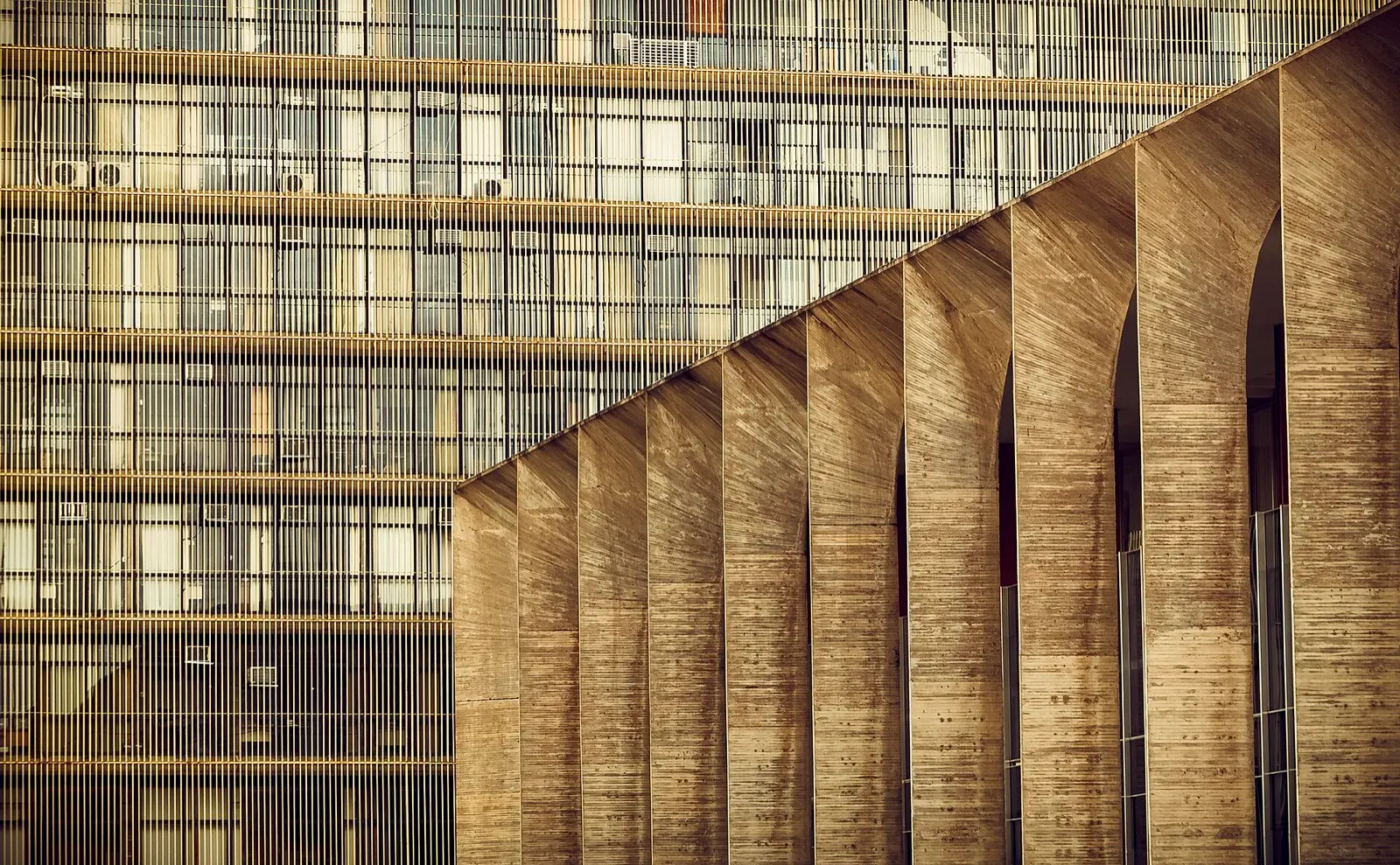 Colunas de concreto em arco da fachada do Palácio do Itamaraty, em Brasília, ao lado de um prédio com fachada de grades verticais.