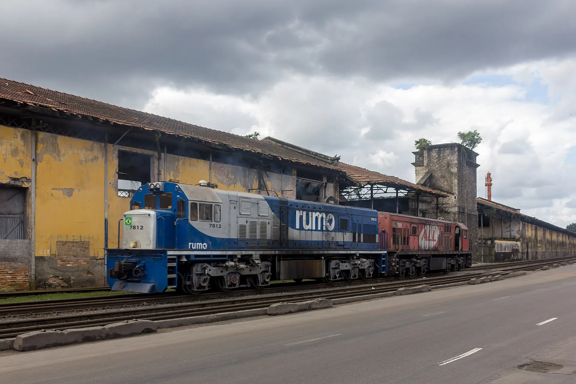 Duas locomotivas de carga em trilhos ao lado de armazéns e de uma via no porto de Santos.